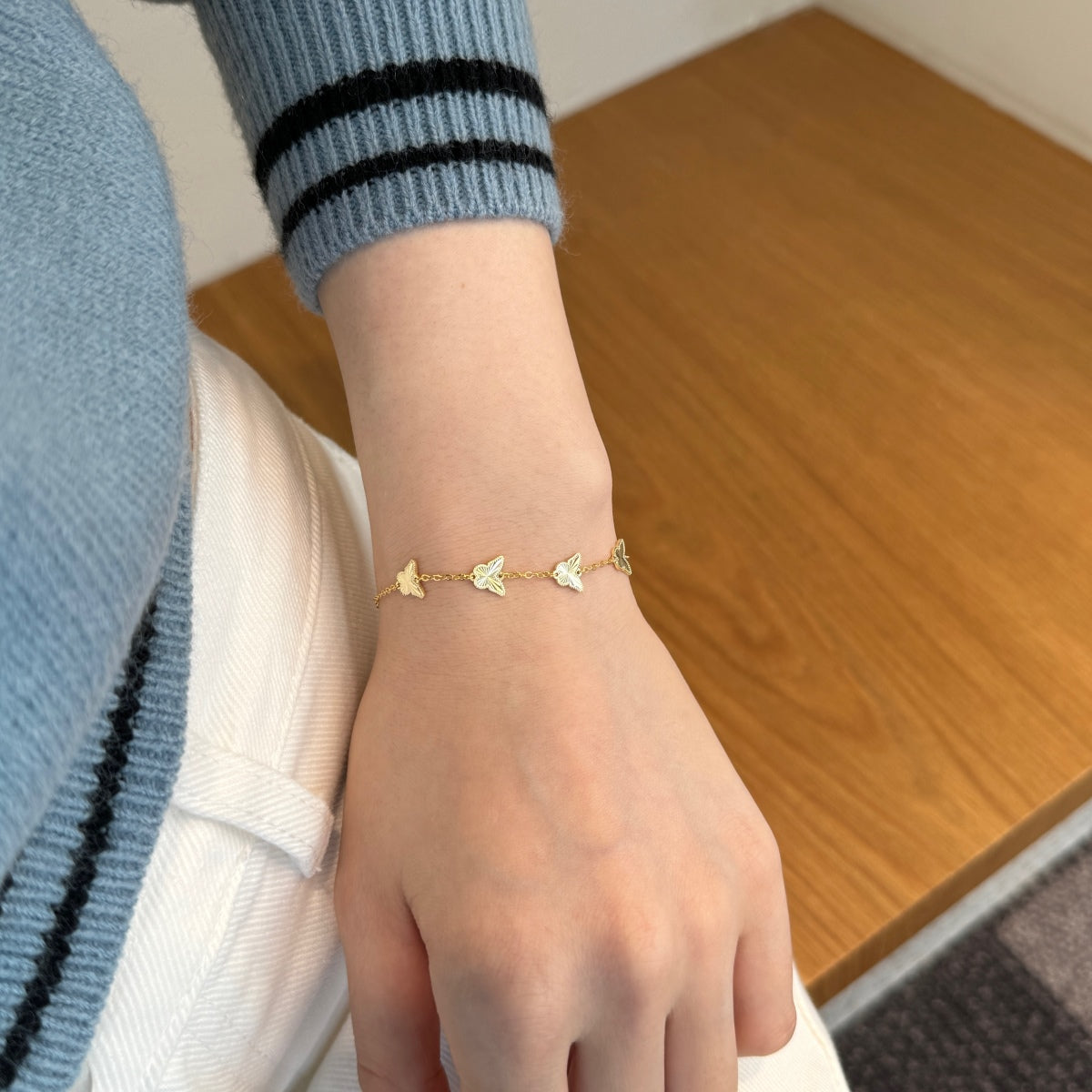 Hand wearing a gold bracelet with butterfly motifs on a wooden surface
