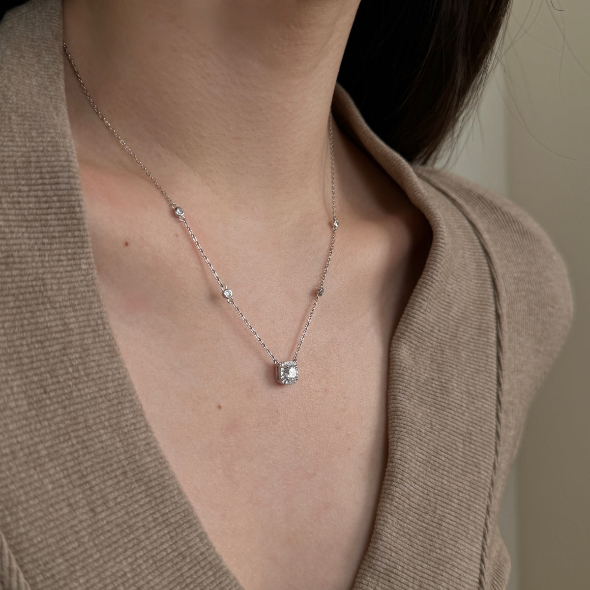 Necklace with a pendant worn by a person in a beige cardigan.