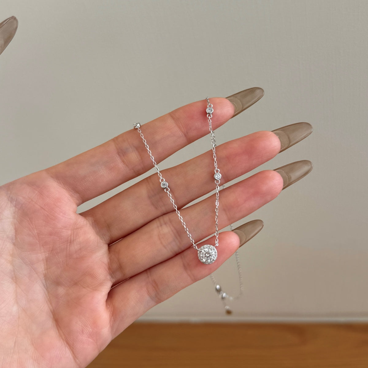 Silver necklace with a diamond pendant held in a hand against a neutral background
