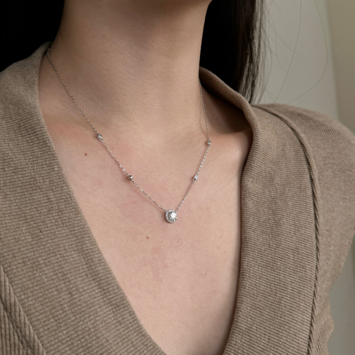 Necklace with a pendant worn by a person in a beige cardigan.