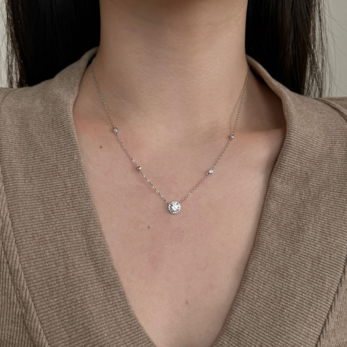 Necklace with a central diamond pendant worn by a person in a brown outfit.