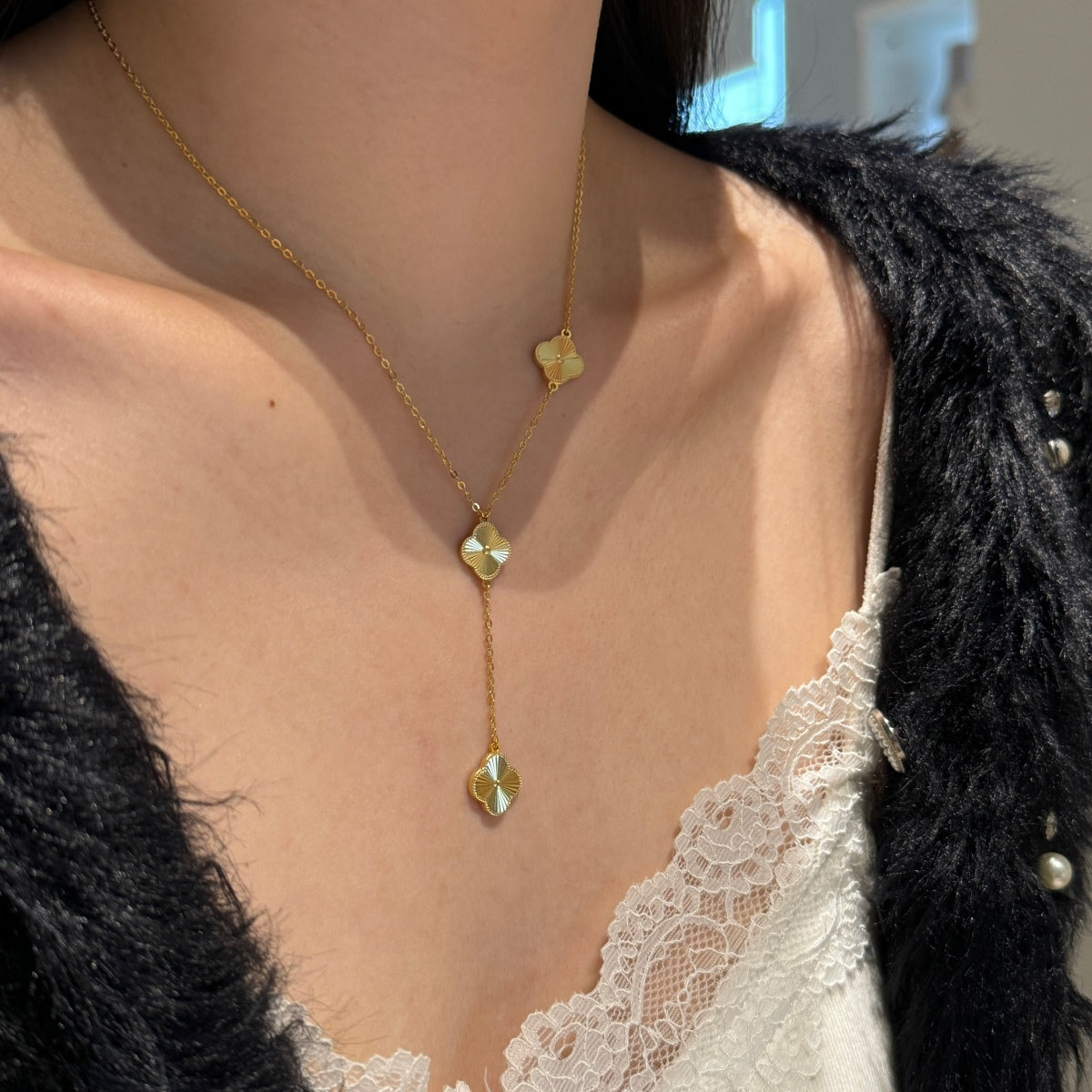  four leaf clover drop Gold necklace with pendant on a person wearing a black jacket and white lace top.
