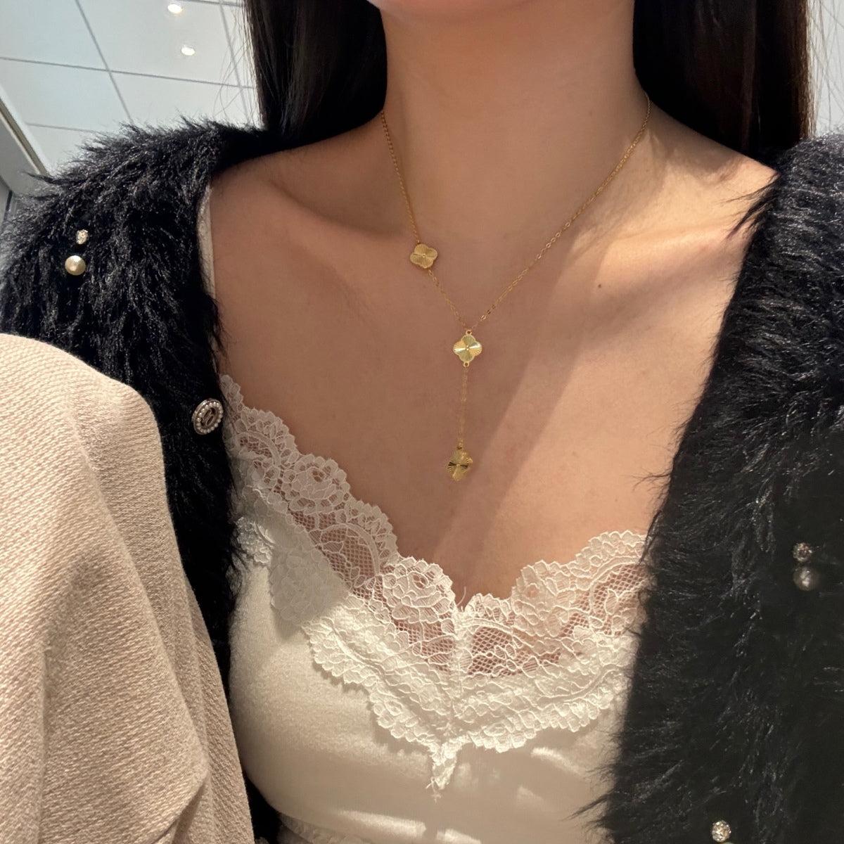 Person wearing a gold  four leaf clover drop necklace with a black jacket and white lace top.