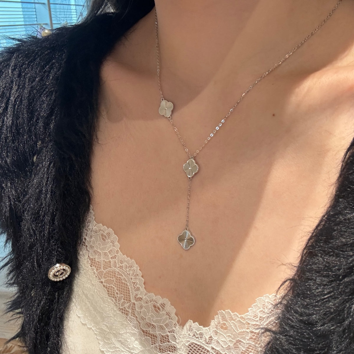 Necklace with four leaf clover pendants worn by a person with black hair and a white lace garment.