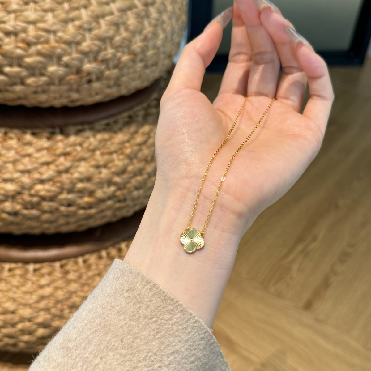 Hand wearing a gold four leaf clover necklace, blurred woven basket in the background