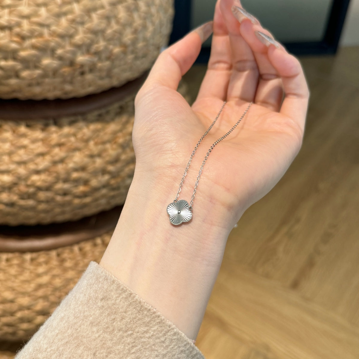 Hand holding a silver necklace with a four leaf clover pendant against a blurred background