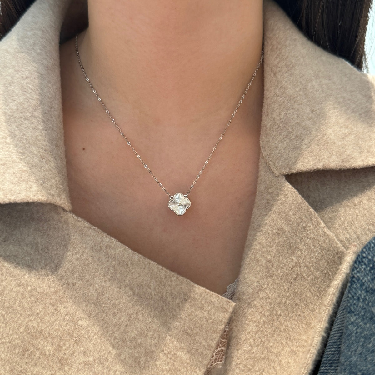 Necklace with a small four leaf clover pendant worn by a person in a beige coat.