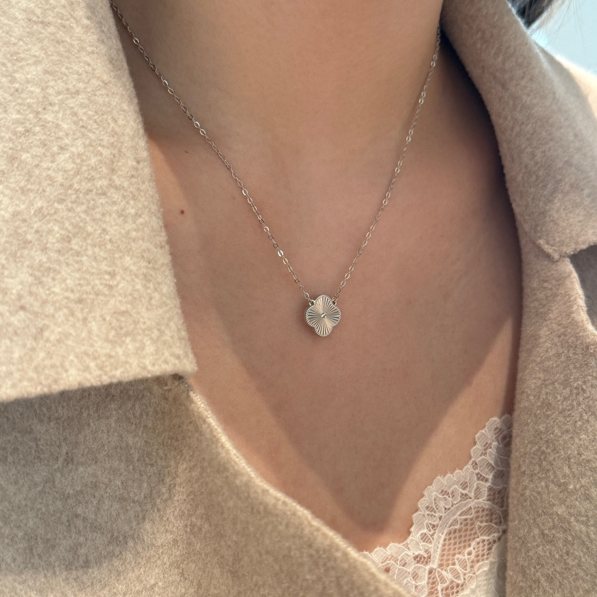 Necklace with a small four leaf clover pendant worn by a person, with a neutral background