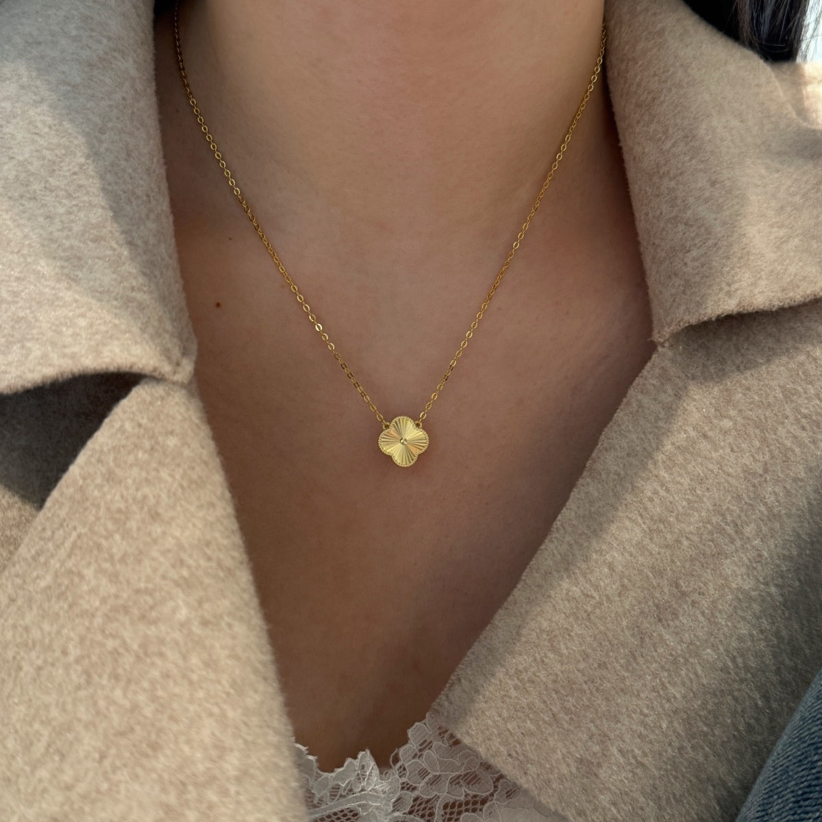 Gold necklace with a four leaf clover pendant worn by a person in a beige coat.