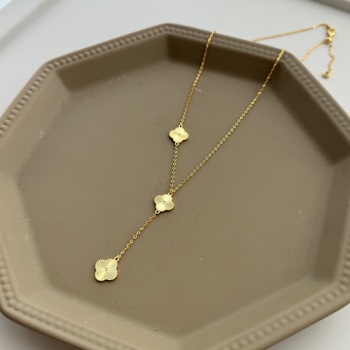 Gold  four leaf clover drop necklace on a beige hexagonal tray