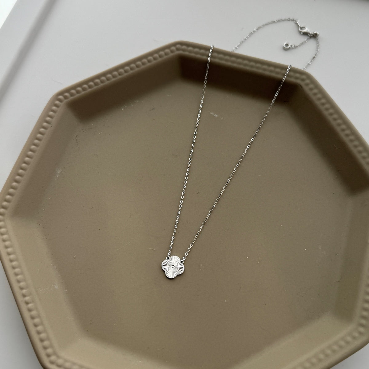 Silver necklace with a four leaf clover pendant on a beige hexagonal tray