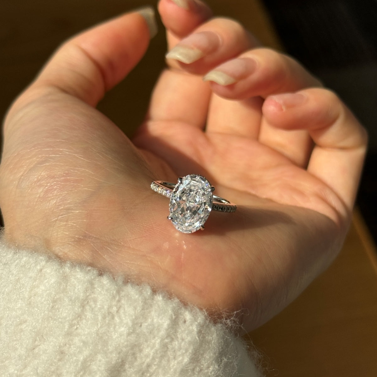 Oval Diamond ring on a person's finger with a blurred background