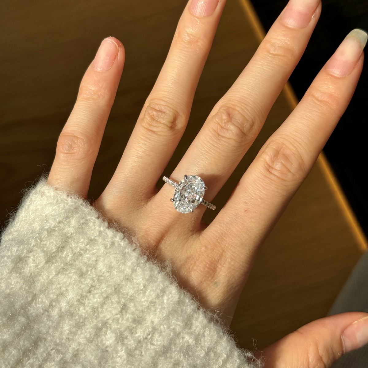 Hand wearing an oval diamond ring with a blurred background