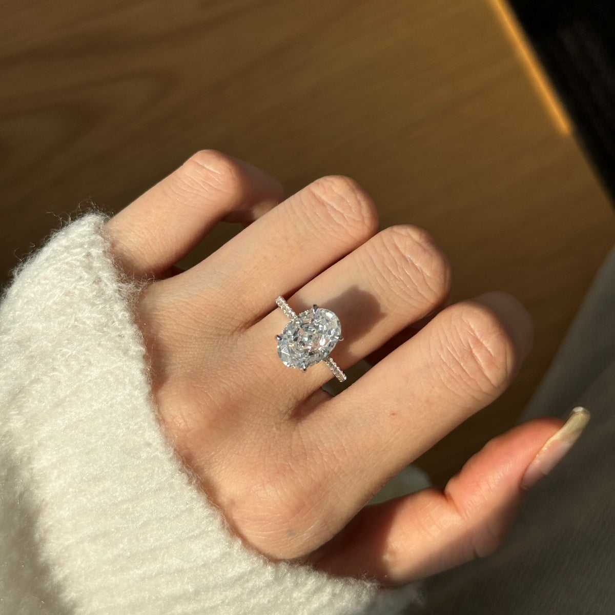 Hand wearing an oval diamond ring on a wooden surface