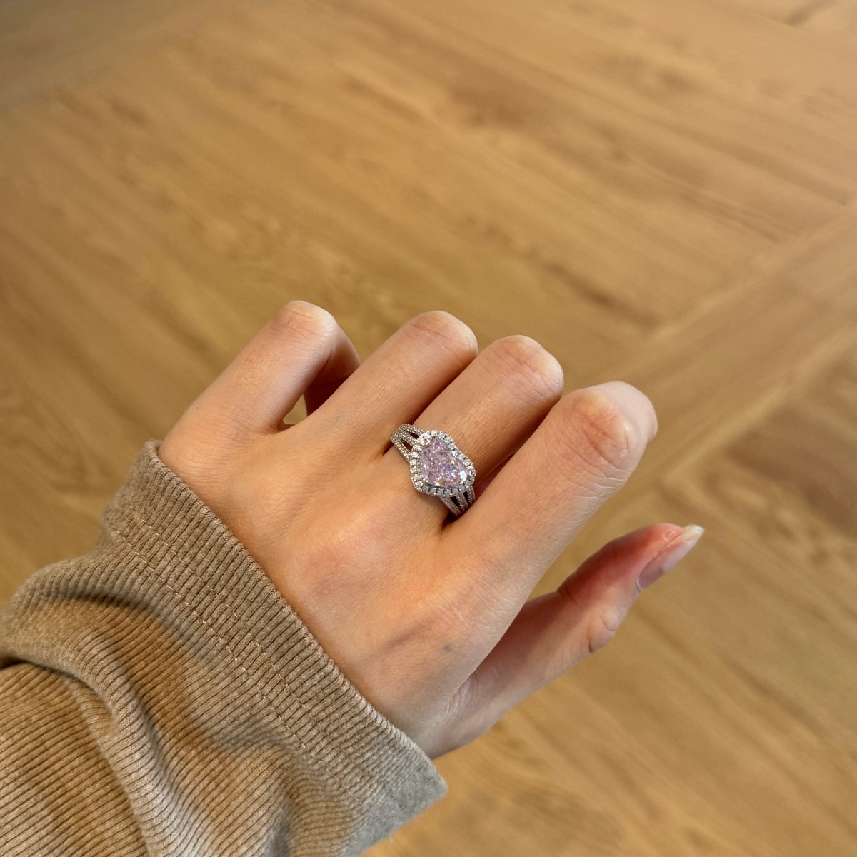 Hand wearing a ring with a pink gemstone on a wooden surface