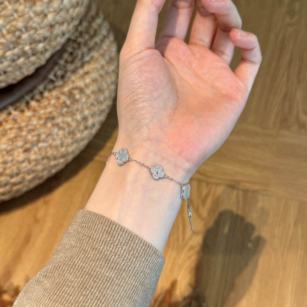 Hand wearing a silver clover bracelet on a wooden surface