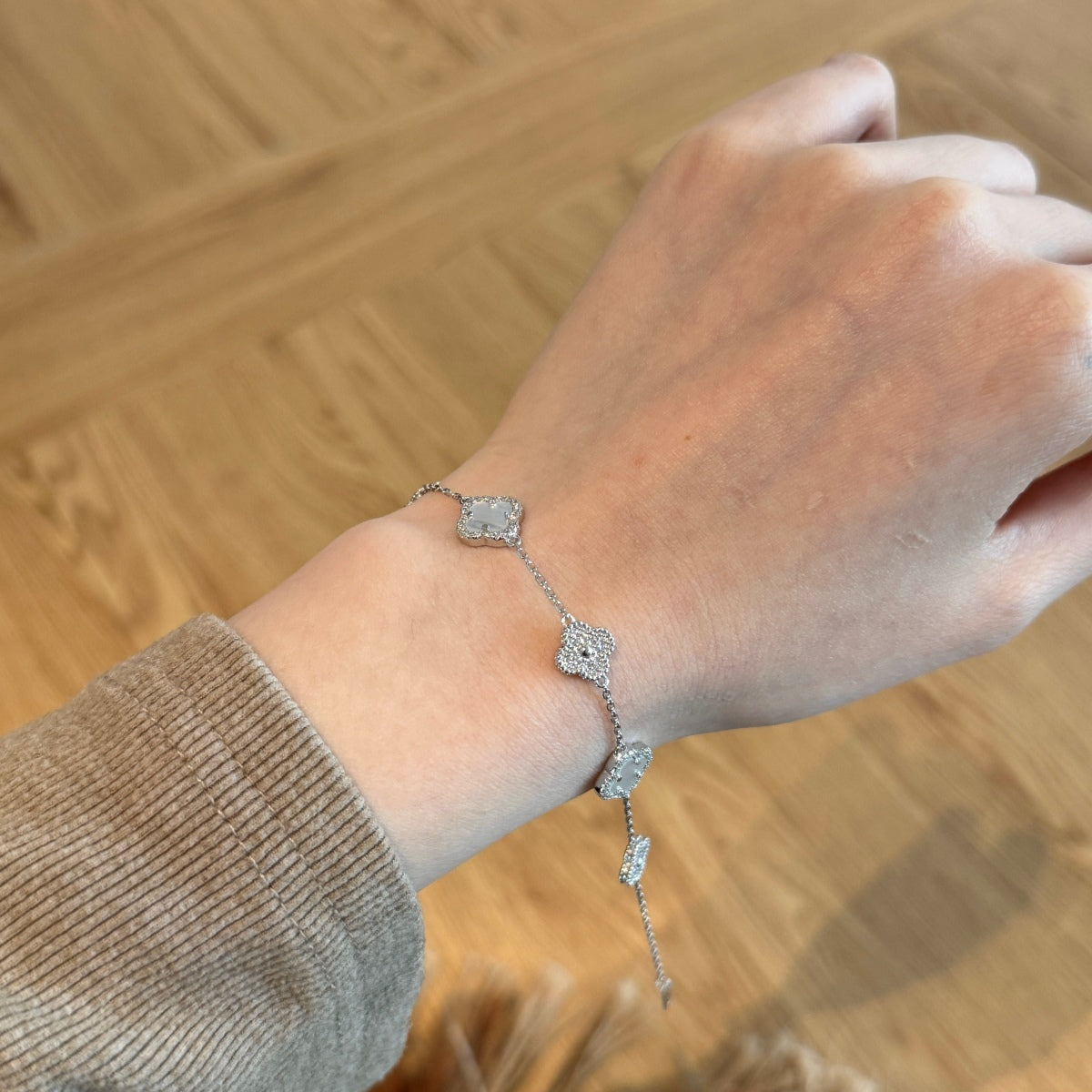 Hand wearing a silver clover leaf bracelet on a wooden surface