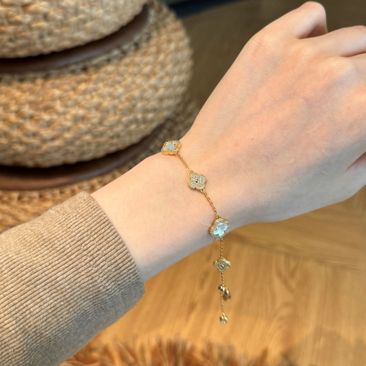 Hand wearing a gold clover bracelet with gemstones on a wooden surface