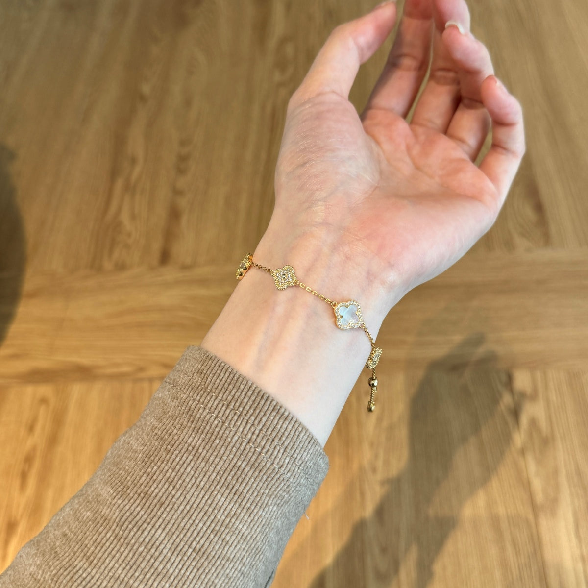 Hand wearing a gold bracelet with flower motifs on a wooden background
