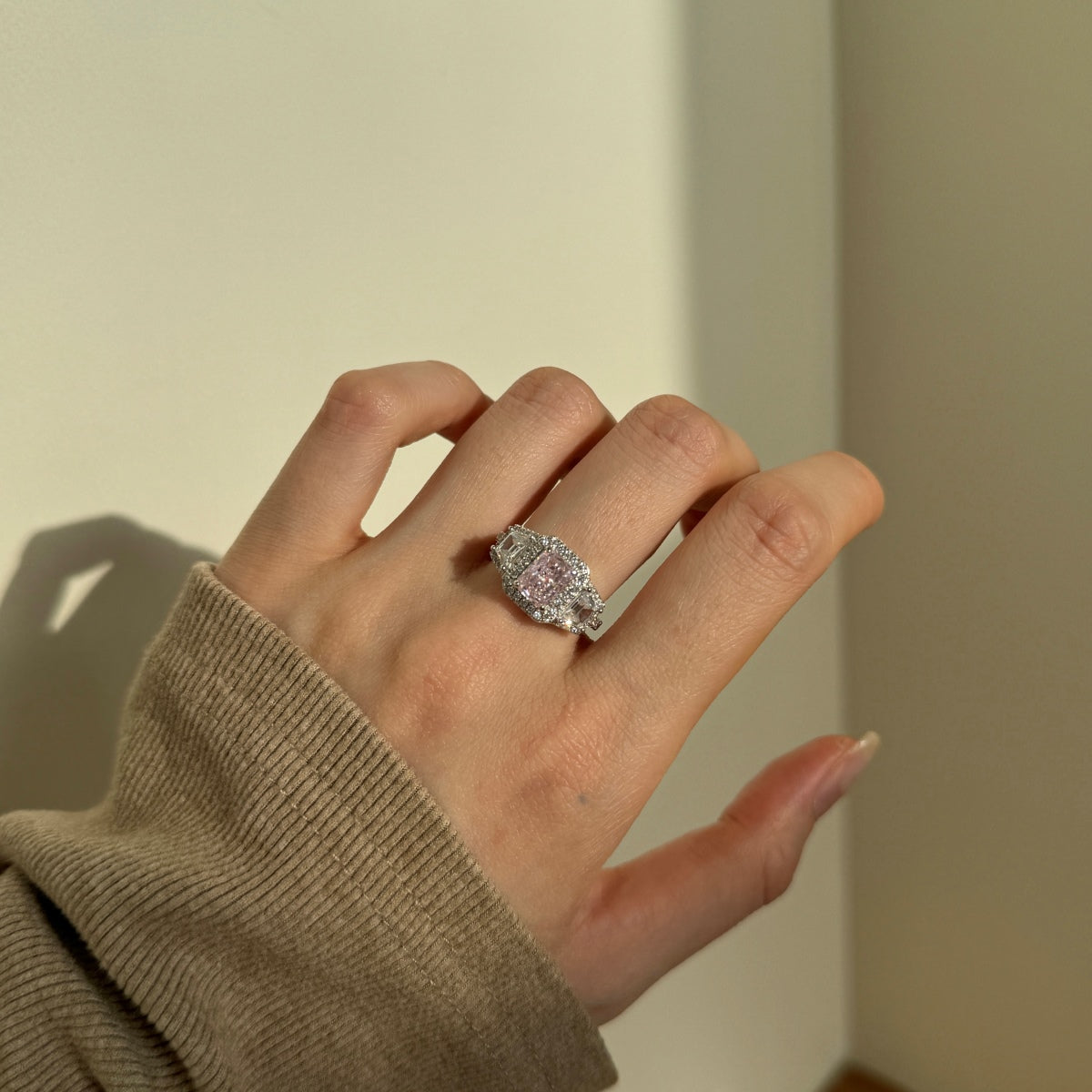 Hand wearing a diamond ring against a neutral background