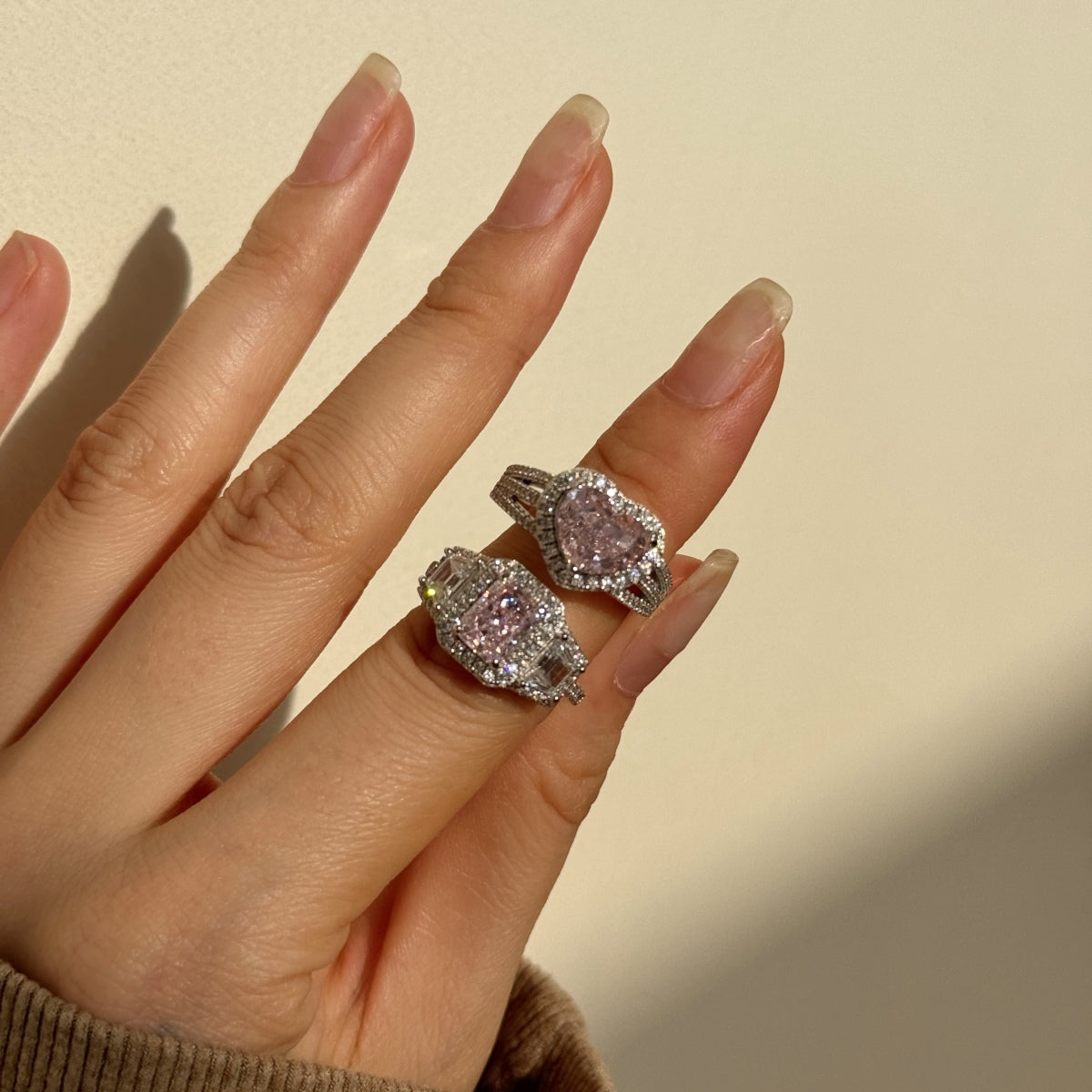 Hand wearing two pink diamond rings on a neutral background