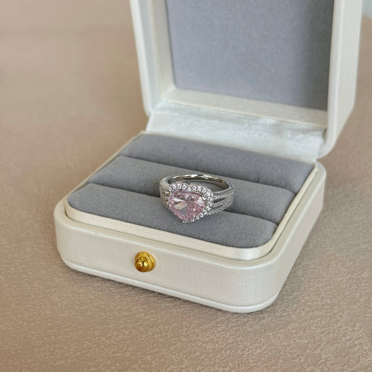 Ring with a pink gemstone in an open jewelry box on a beige surface