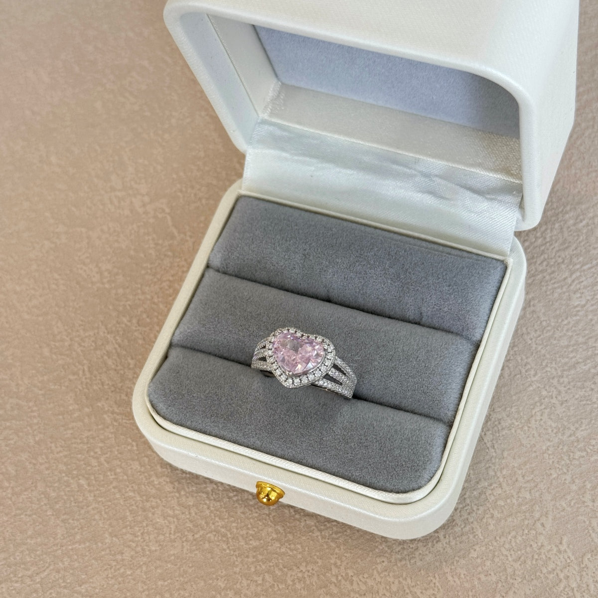Pink gemstone heart ring in a jewelry box on a beige surface