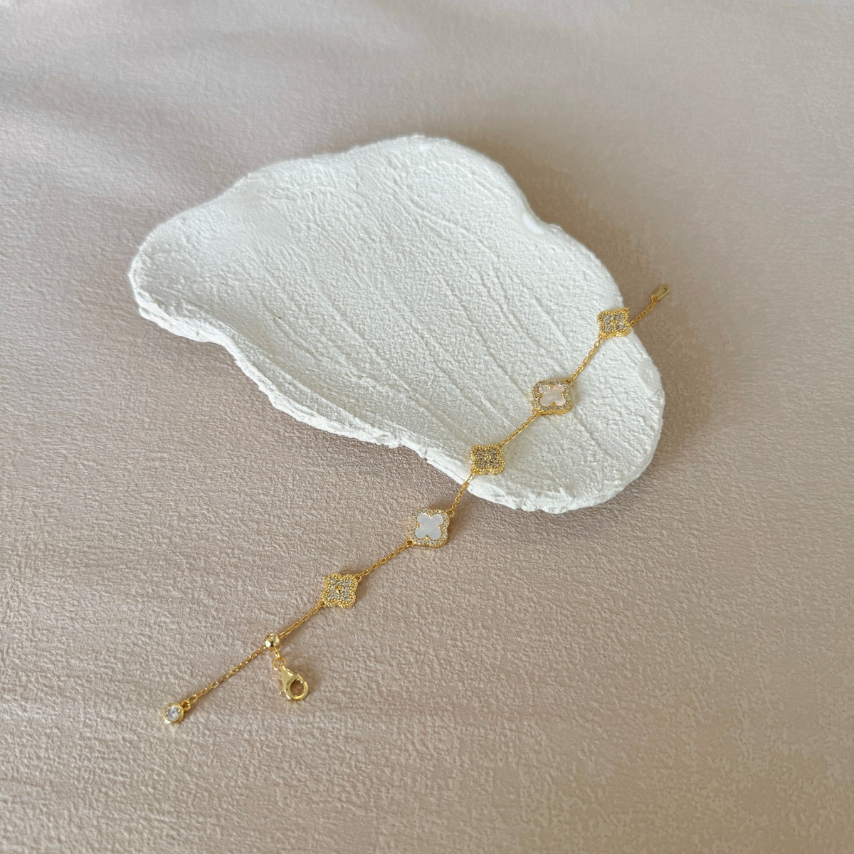 Gold flower motif bracelet with a white stone on a beige surface