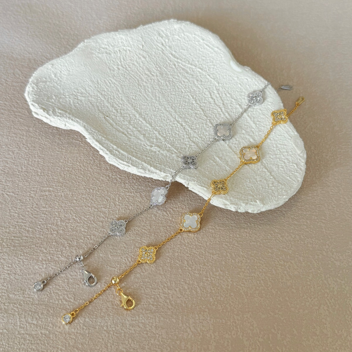 Gold and silver clover bracelets on a white stone surface