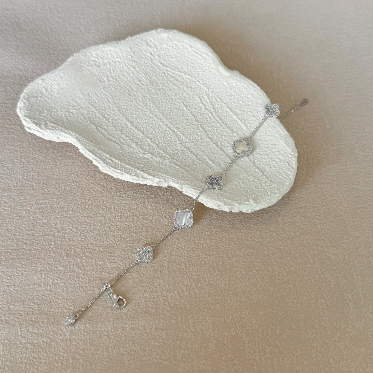 Silver clover bracelet with diamond-like stones on a beige surface