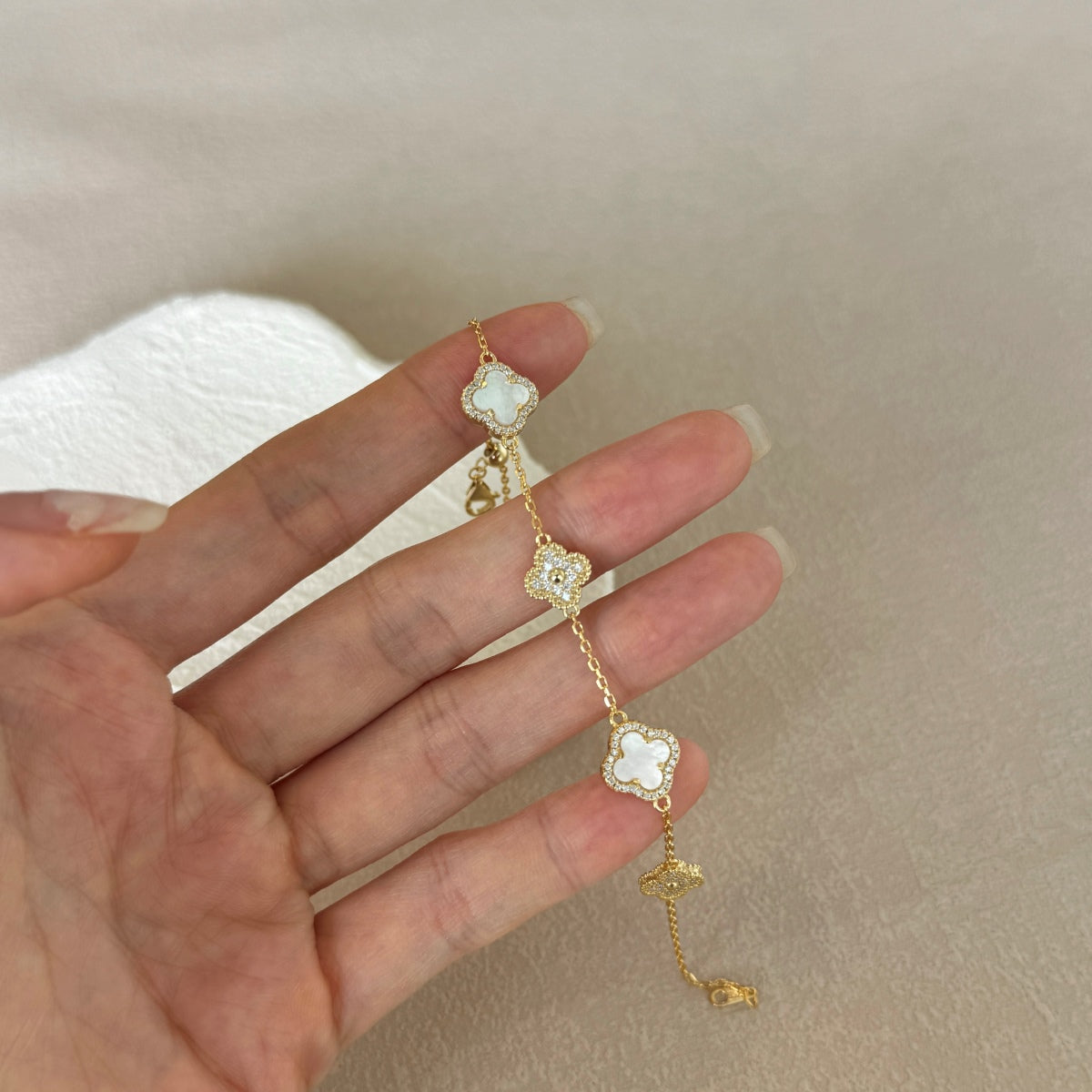 Gold clover bracelets with floral designs on a hand against a neutral background