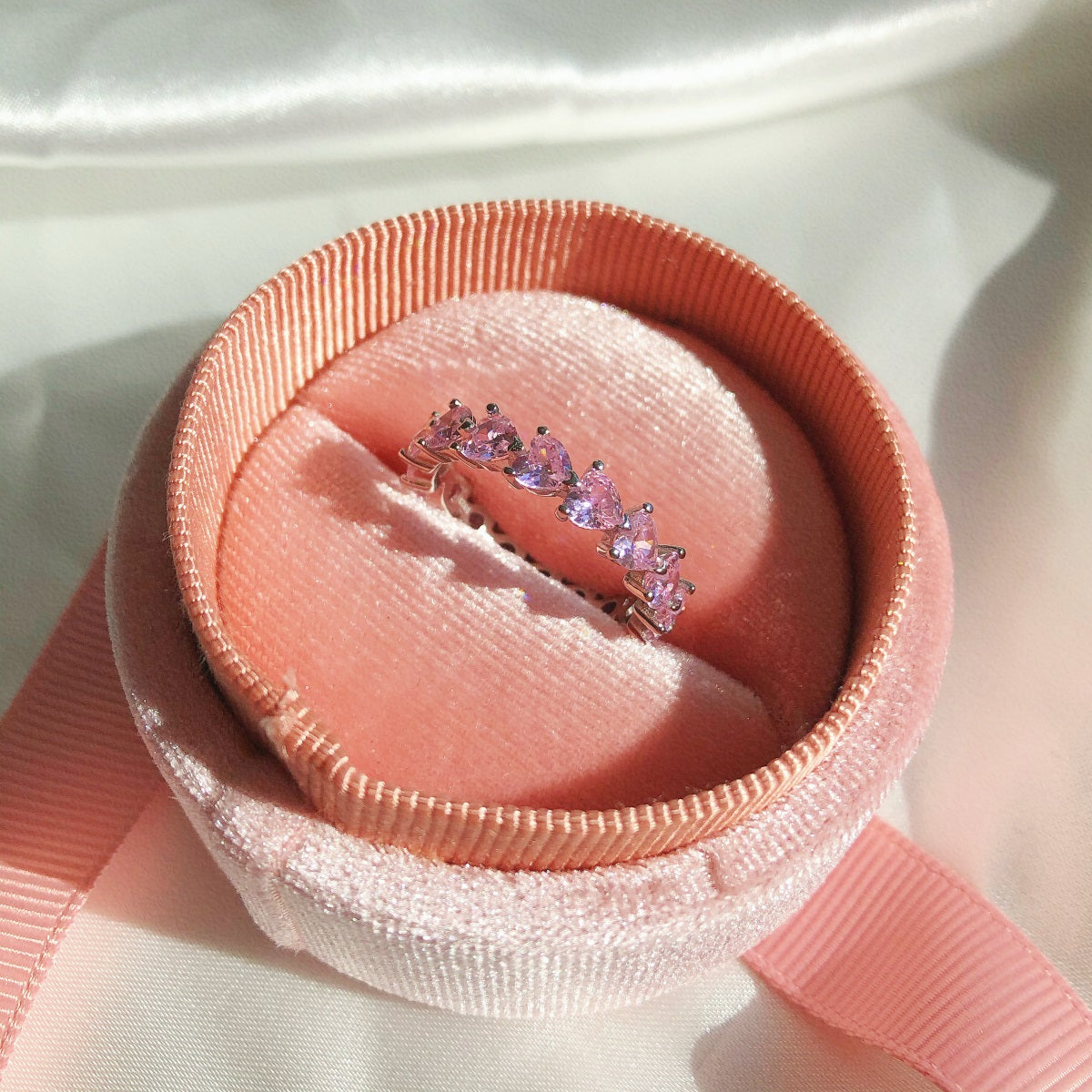 Ring with pink gemstones in a pink jewelry box on a white fabric background