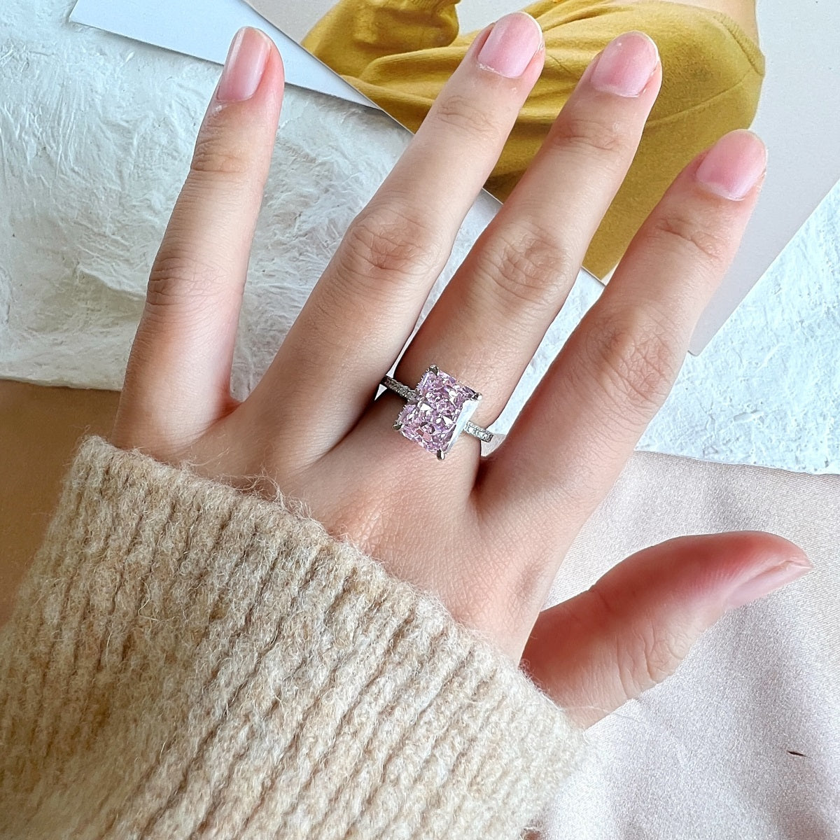 Hand wearing a pink diamond ring on a neutral background
