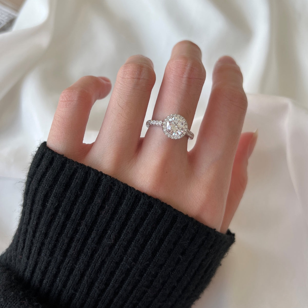Hand wearing a diamond ring on a plain background