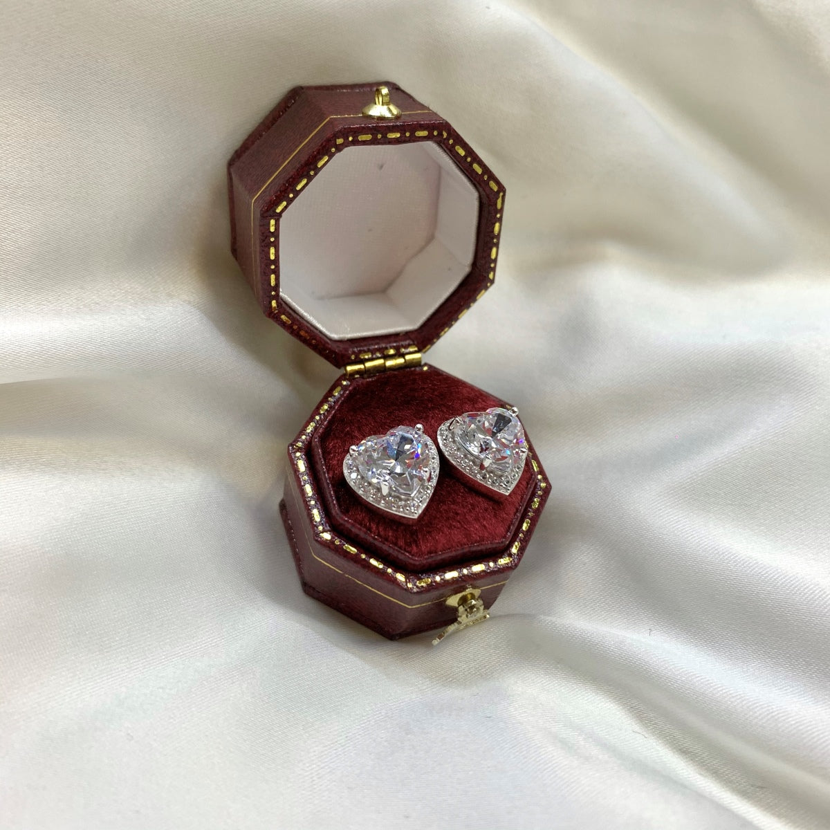Heart-shaped diamond earrings in a red jewelry box on a white fabric background
