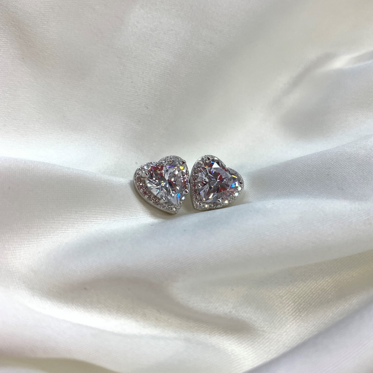 Heart-shaped diamond earrings on a white satin background