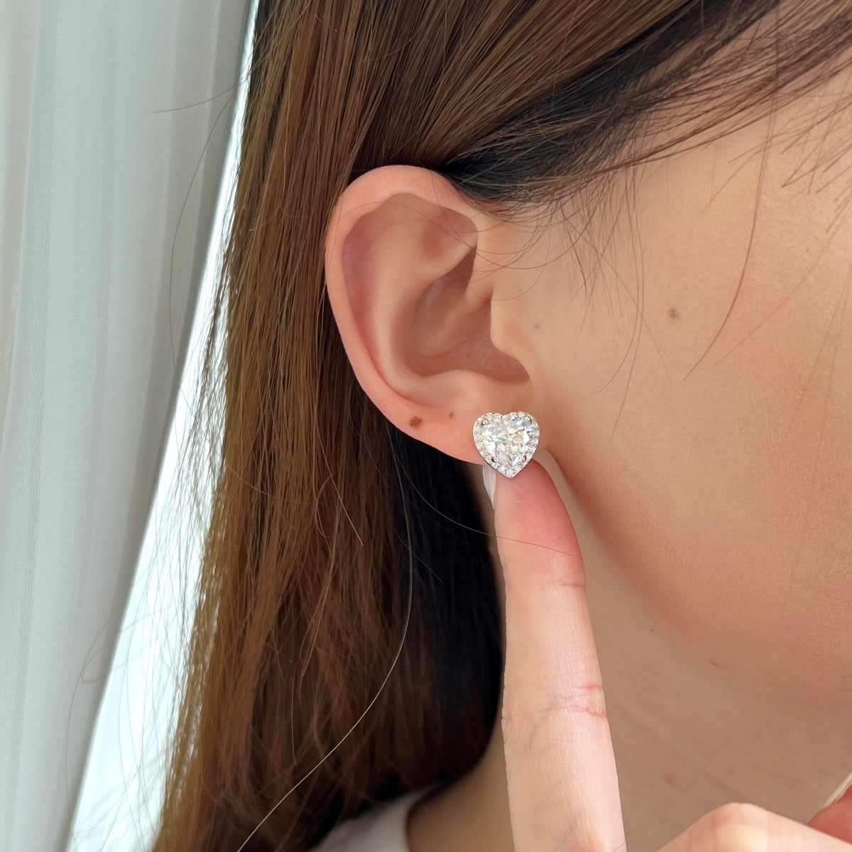 Heart-shaped diamond earring worn by a person with brown hair.