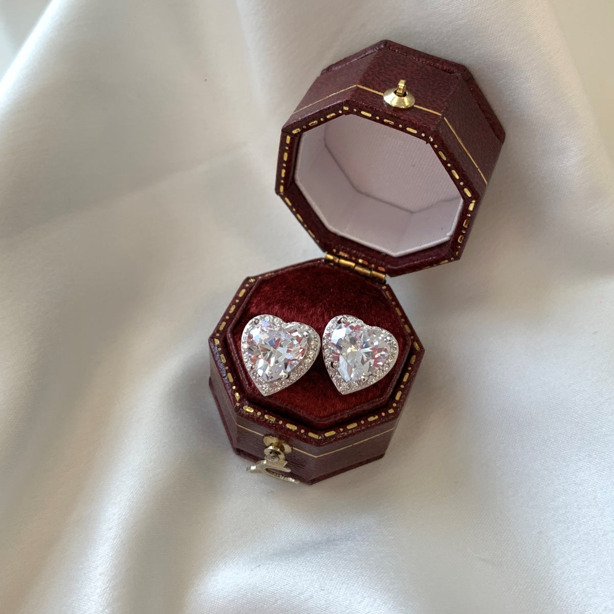 Heart-shaped diamond earrings in a brown jewelry box on a white background
