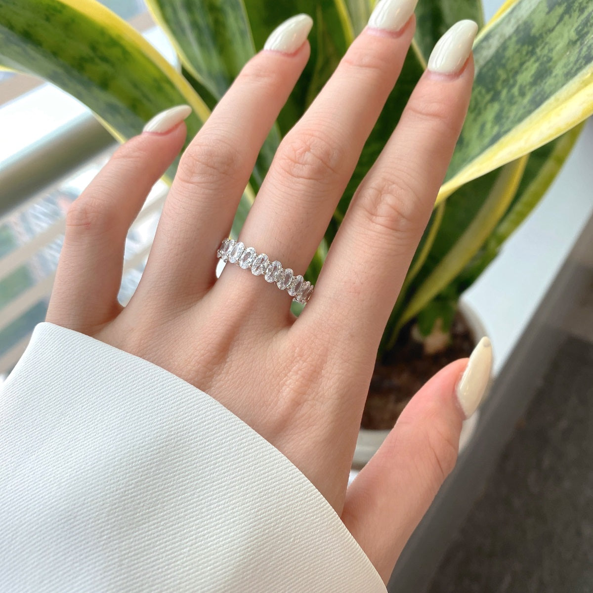 Hand wearing a silver ring with a plant in the background