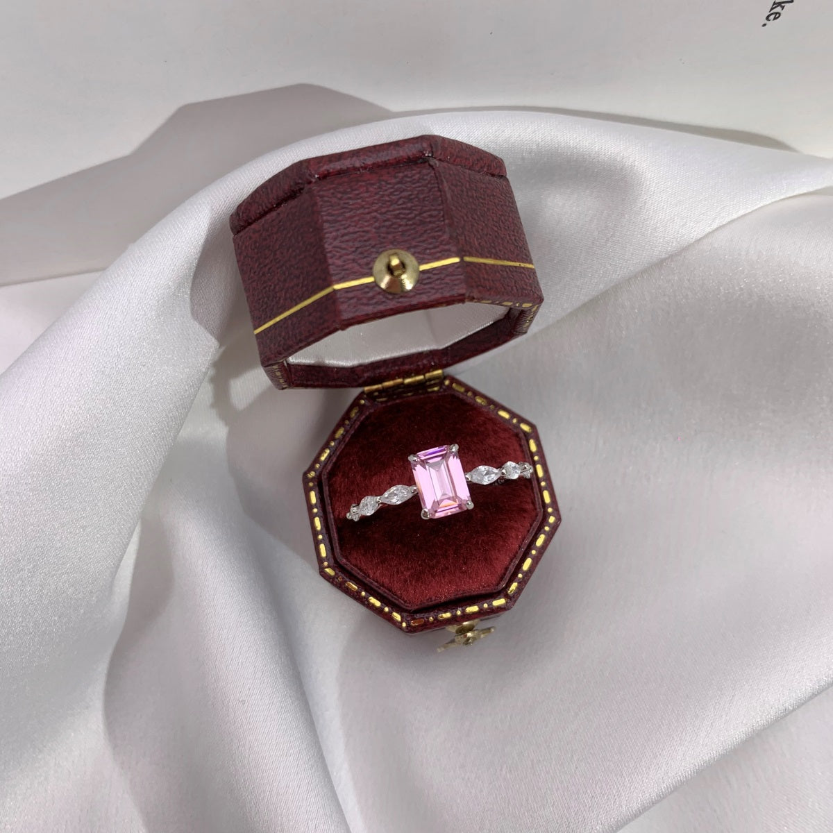 Pink gemstone ring in a red velvet box on white fabric