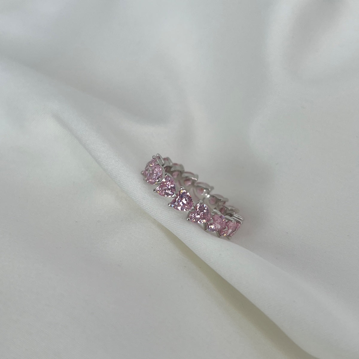 Silver ring with pink gemstones on a white fabric background