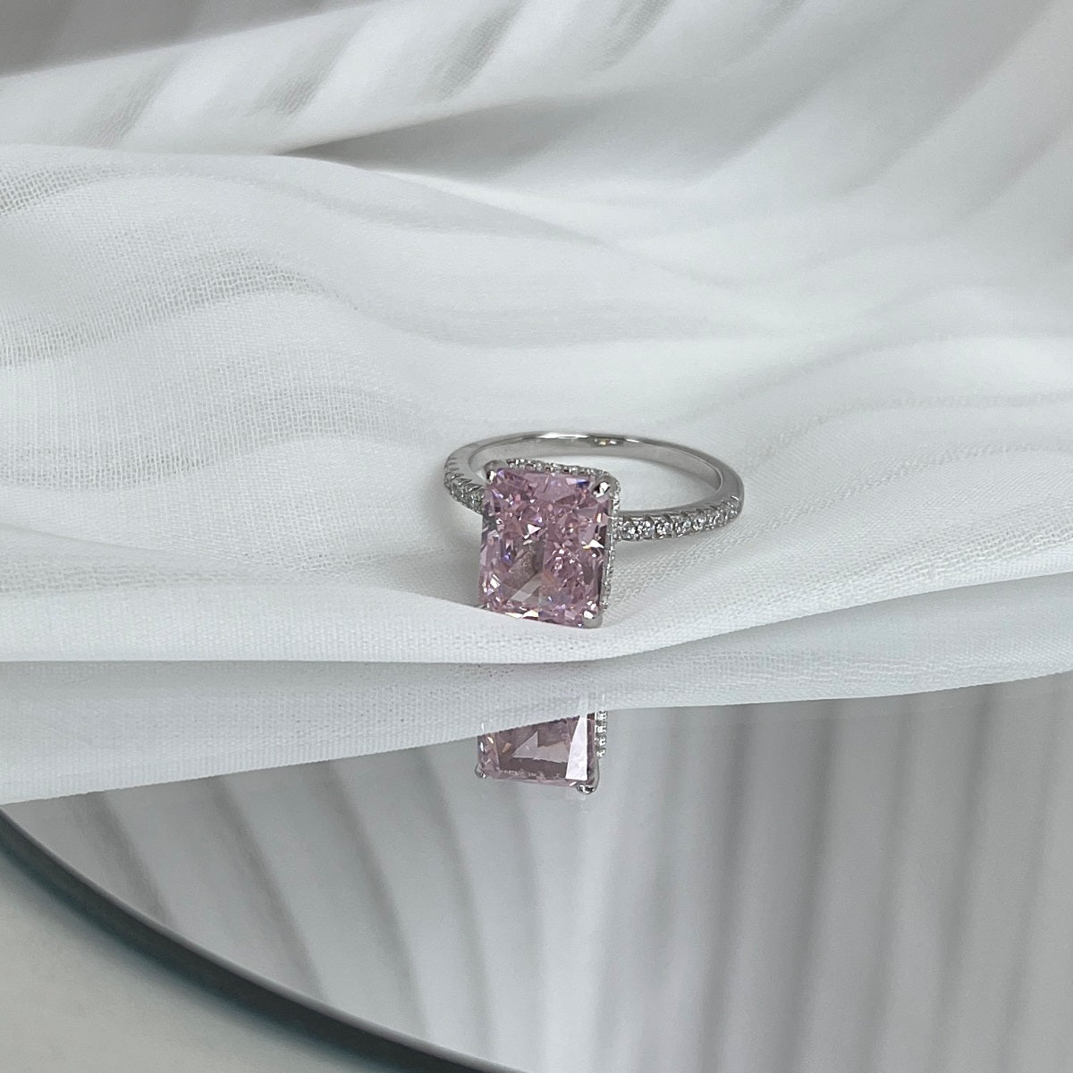 Pink radiant cut diamond ring on a white fabric background