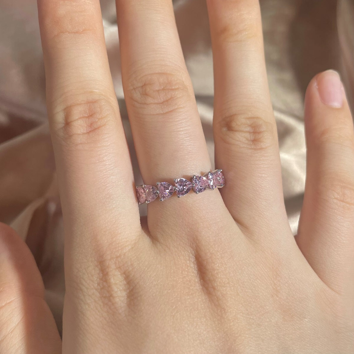 Pink gemstone ring on a hand with a soft pink background