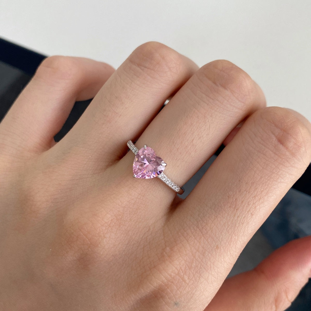 Heart-shaped pink gemstone ring on a hand against a neutral background
