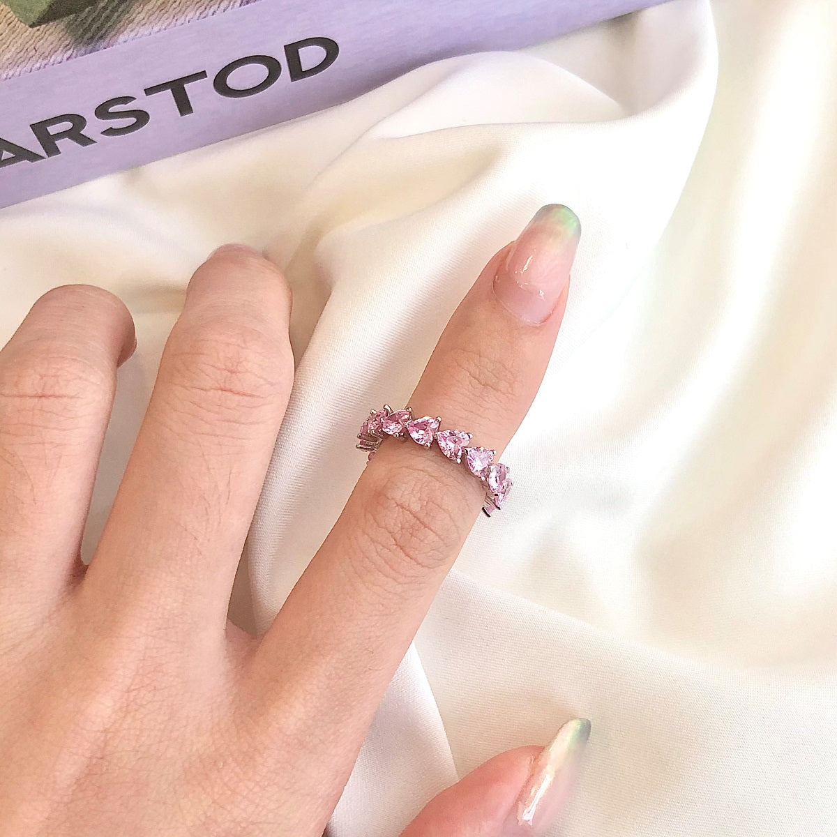Hand wearing a pink ring on a white fabric background