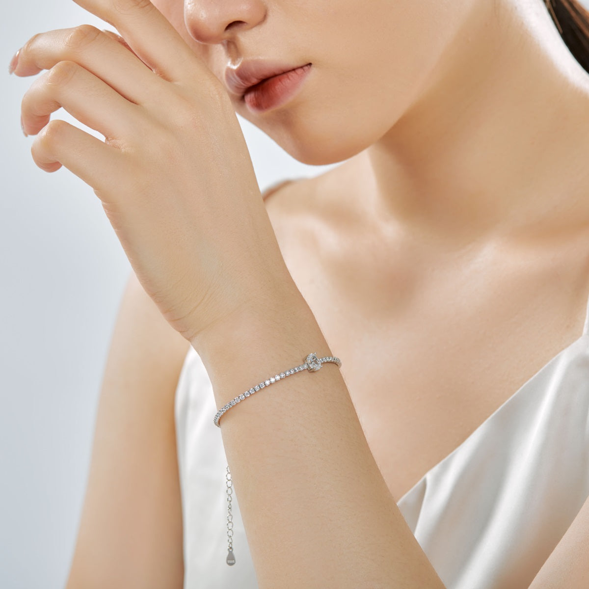 Close-up of a woman's wrist wearing a delicate tennis bracelet on a light background
