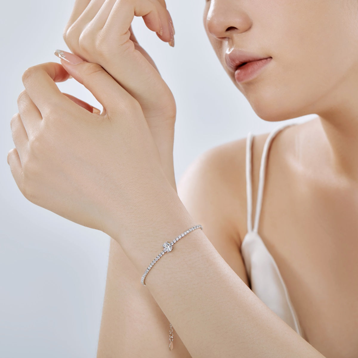 Woman wearing a silver diamond tennis bracelet on a light background