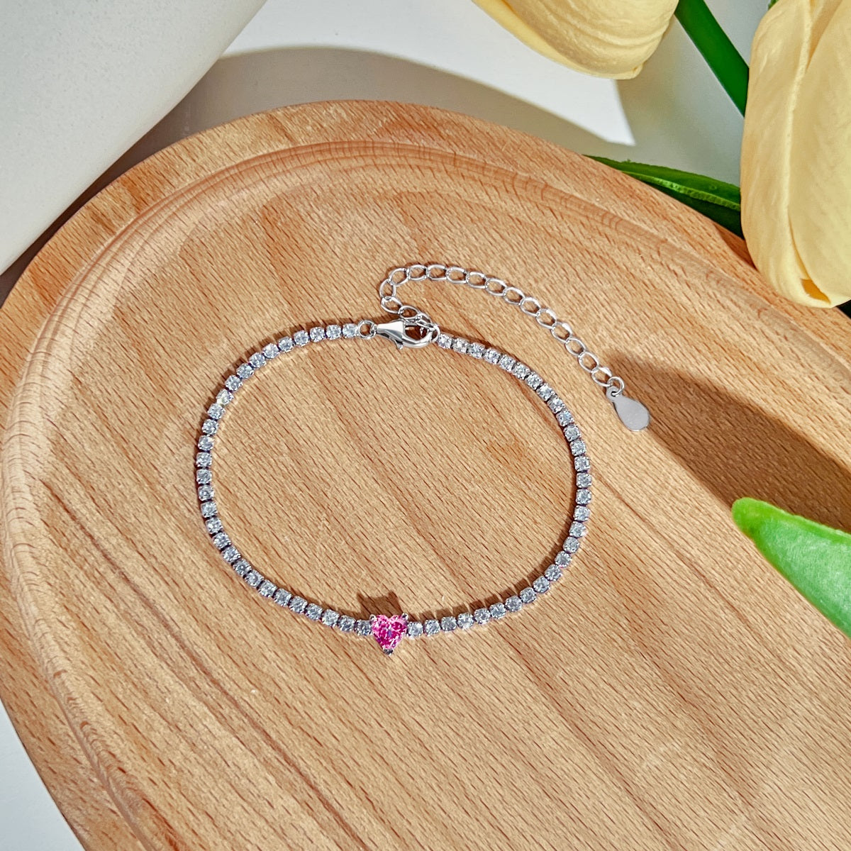 Silver tennis bracelet with a pink heart charm on a wooden surface
