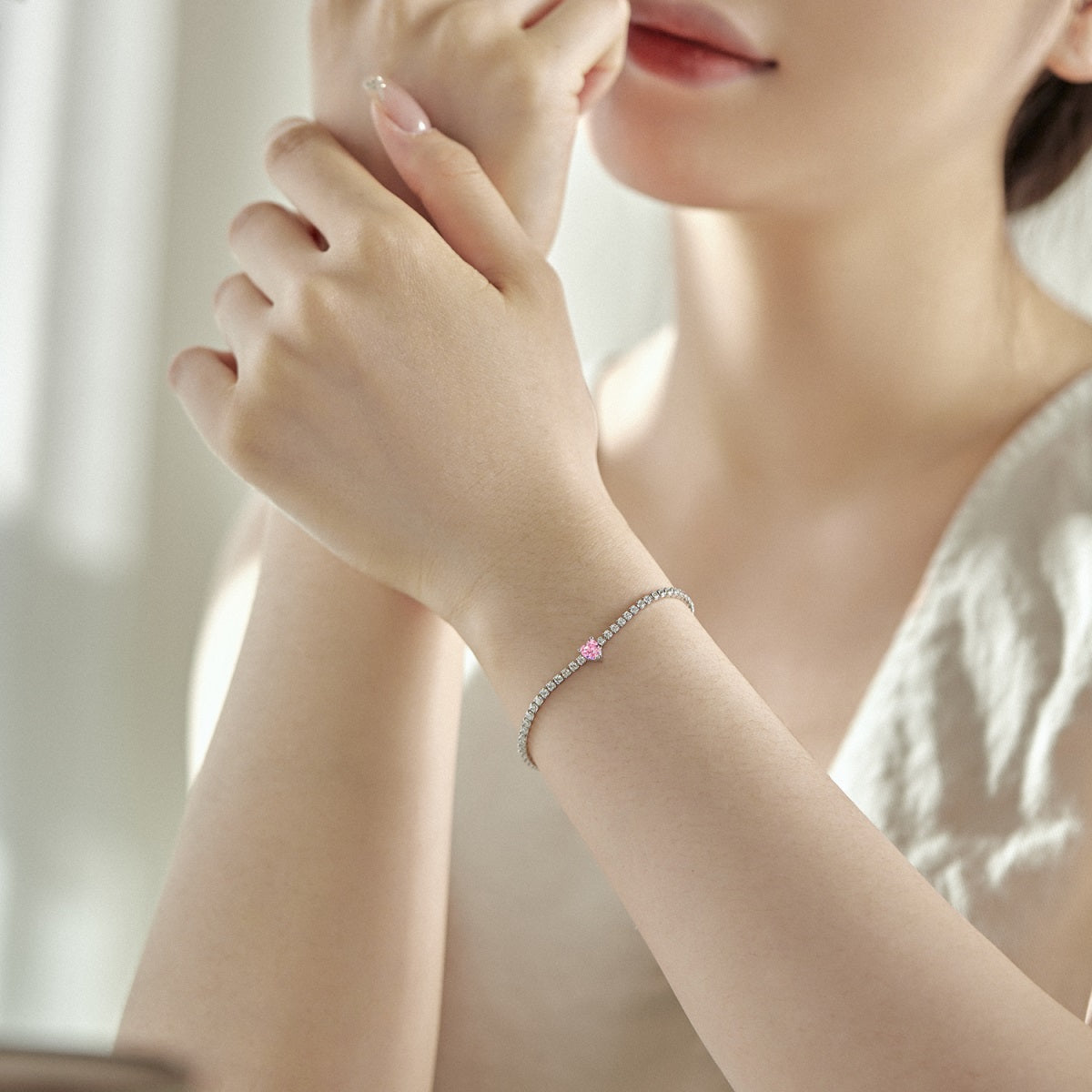 Close-up of a person wearing a bracelet with a pink gemstone, holding their hand to their face.