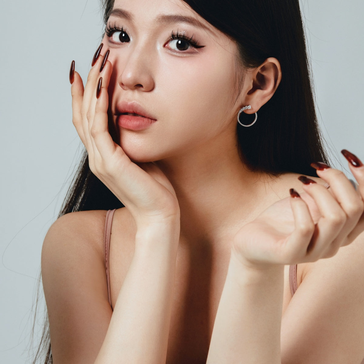 Woman with long dark hair and hoop earrings posing against a light gray background